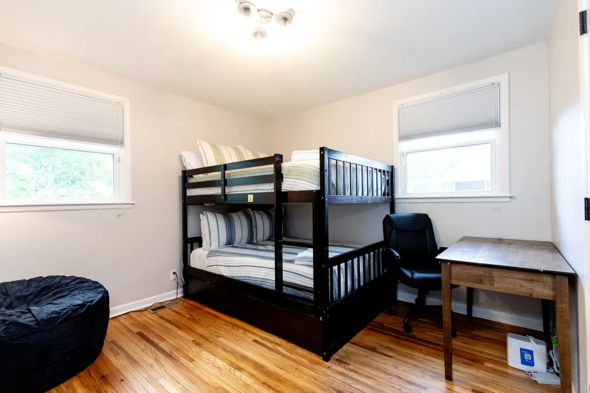 A cheerful, kid-friendly room featuring a bunk bed, bright bean bag chair, desk, and large windows letting in natural light. The playful yet practical setup is ideal for families with children, supporting sleepovers, relaxation, and quiet study time after a day out.