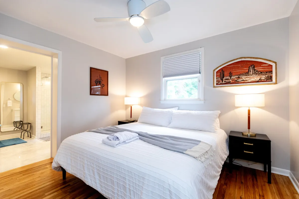 A serene bedroom with a large, comfortable bed dressed in plush linens, flanked by elegant nightstands and calming artwork on the wall. Natural light streams through the window, creating a tranquil atmosphere ideal for relaxation and restful sleep.