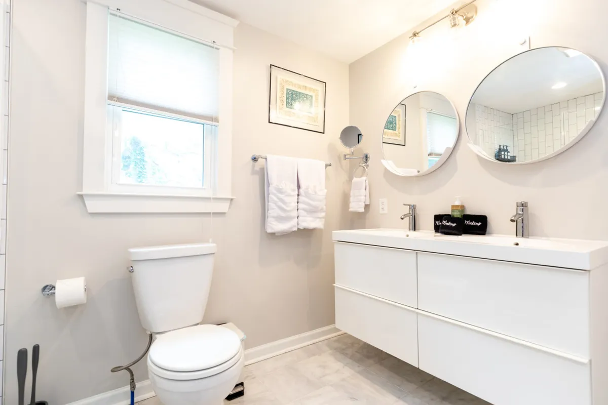 A serene entryway or transition area featuring a vanity with mirrors, neatly folded white towels, and calming artwork on the wall. The tidy, inviting space sets a tone of comfort and attention to detail.