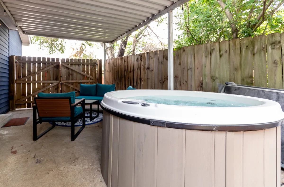 A serene backyard angle that highlights the hot tub and a dedicated seating area, framed by a privacy fence. The tranquil environment is ideal for morning coffee or unwinding after a long day.