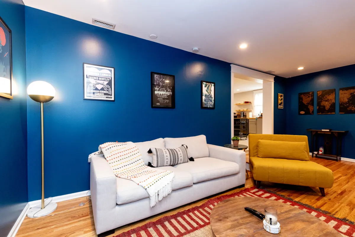 A cozy, stylish living room featuring a plush sofa, a vibrant yellow chair, a coffee table, wall art, and a lamp, arranged to encourage relaxation and group gatherings. The welcoming atmosphere is ideal for hosting movie nights or sharing stories after a day exploring Nashville.
