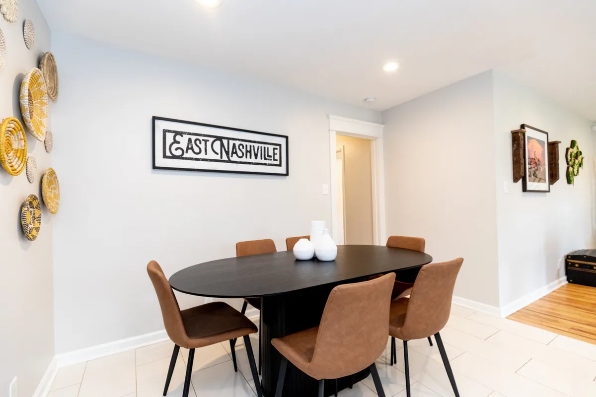 A welcoming dining area anchored by a large table, modern wall art, and an 'East Nashville' sign. The space is set up for shared meals, social gatherings, and lively conversations.