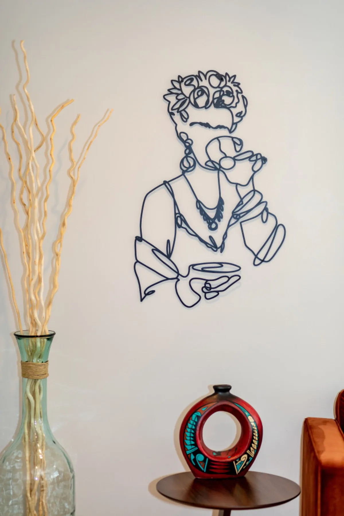 A cozy nook featuring wire art depicting a person holding a drink, decorative vases, and colorful pottery. The setting encourages relaxing with friends, enjoying beverages, and admiring unique artistic touches.